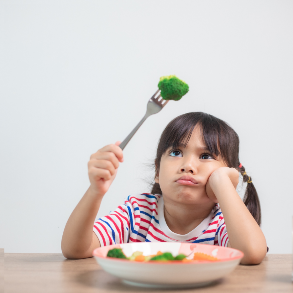 Picky eater at kitchen table looking at a piece of broccoli on her fork